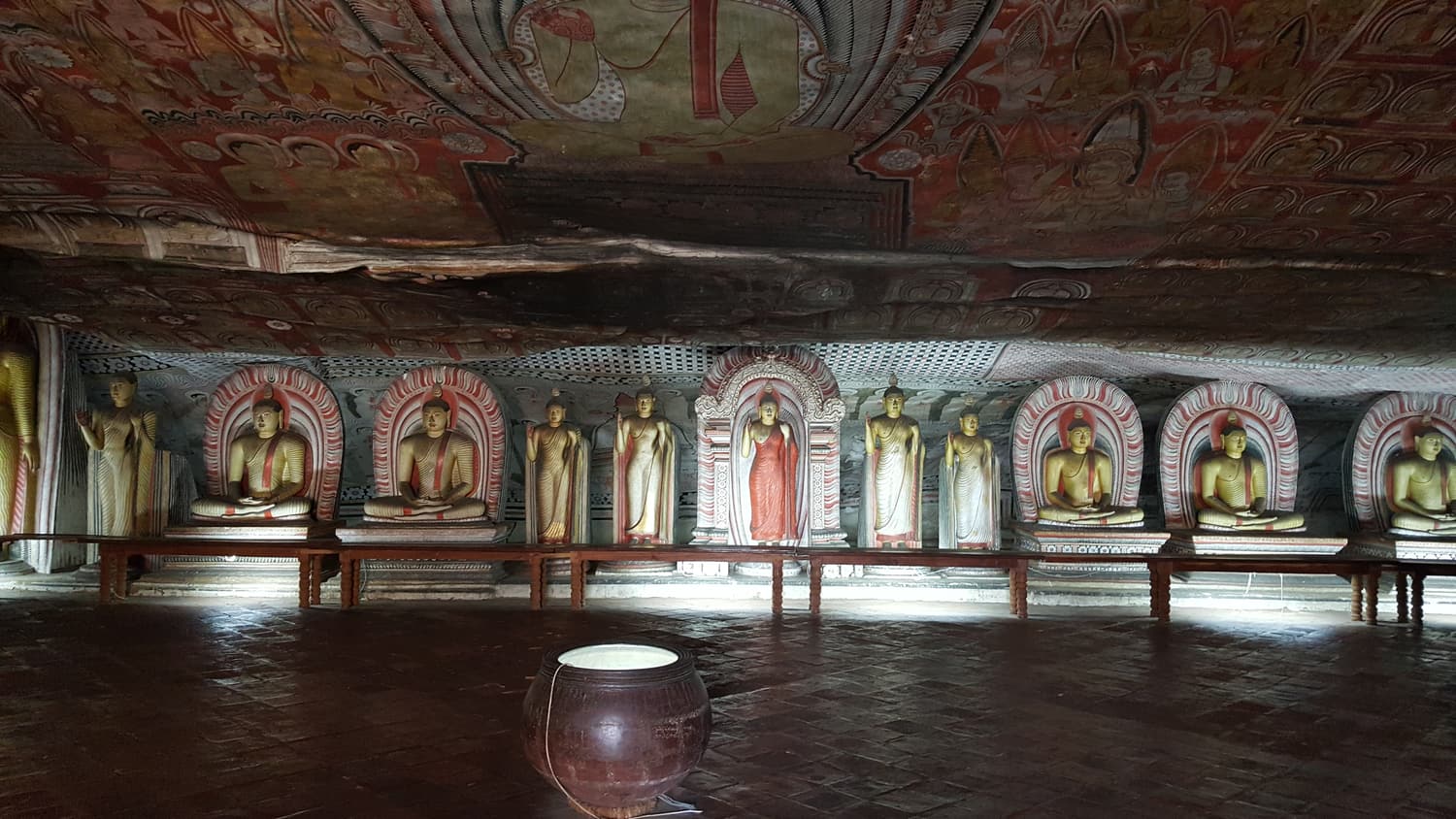 Rows of painted Buddha statues beneath the frescoed ceiling of a Dambulla cave