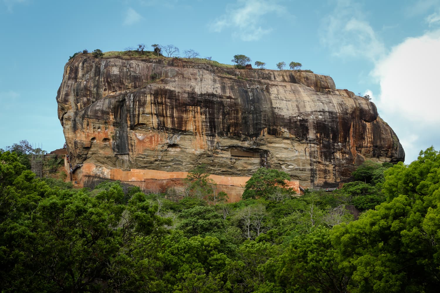 The sheer orange-red walls of Sigiriya Lion Rock rising above the forest