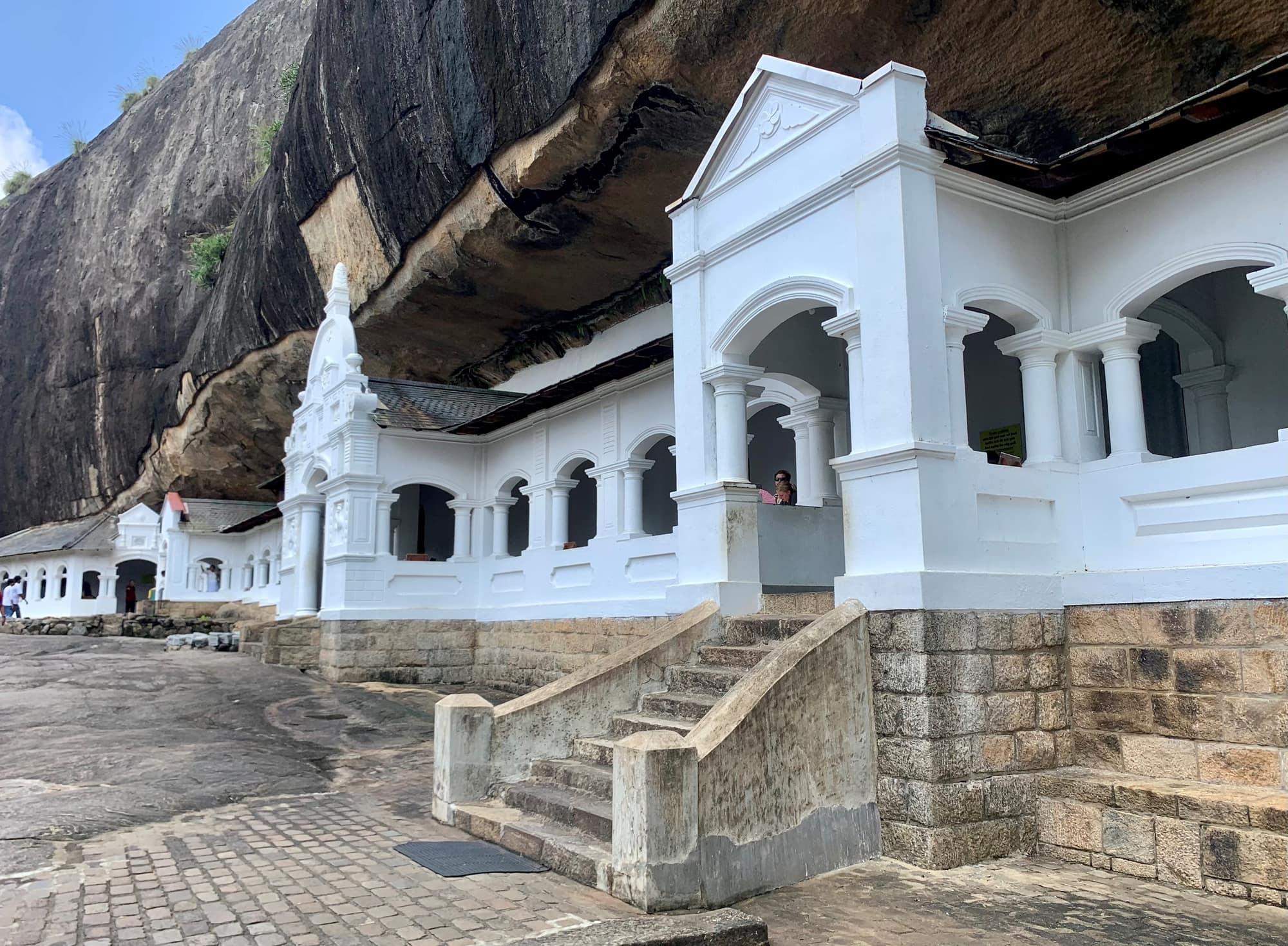 The white colonnaded facade of the Dambulla Cave Temple beneath its huge granite overhang